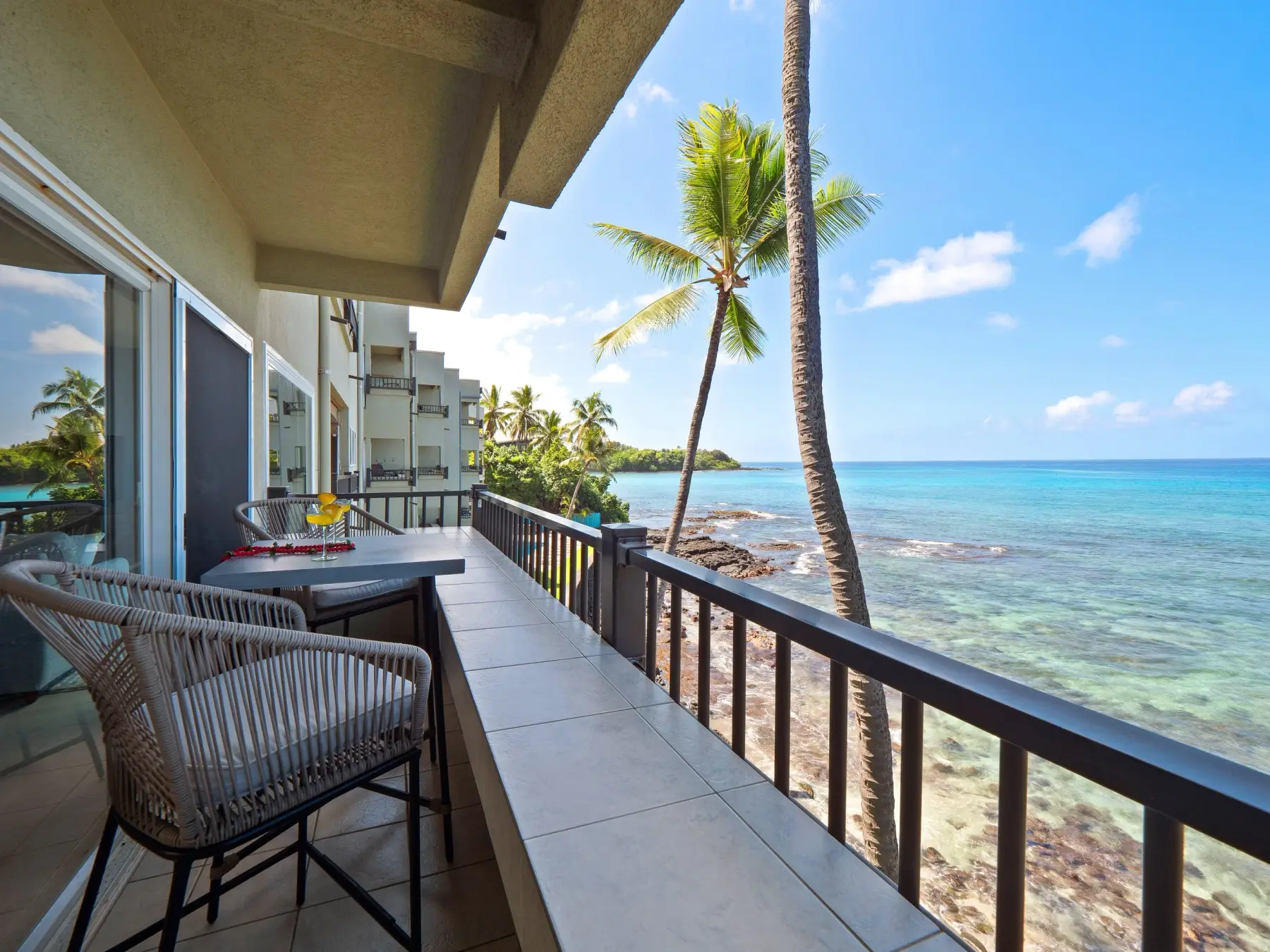 The wrap-around lanai of Unit 300, looking past a palm to the turquoise reef and open Pacific