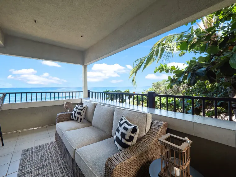Covered lanai with wicker sofa and ocean view through palms